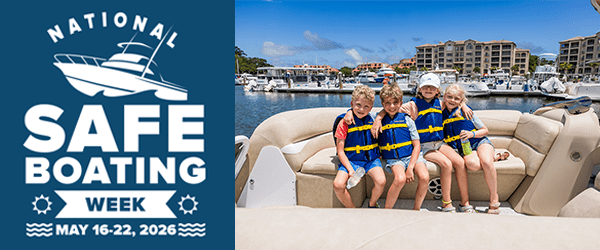 Four kids in life vests on a boat, next to a National Safe Boating Week sign.