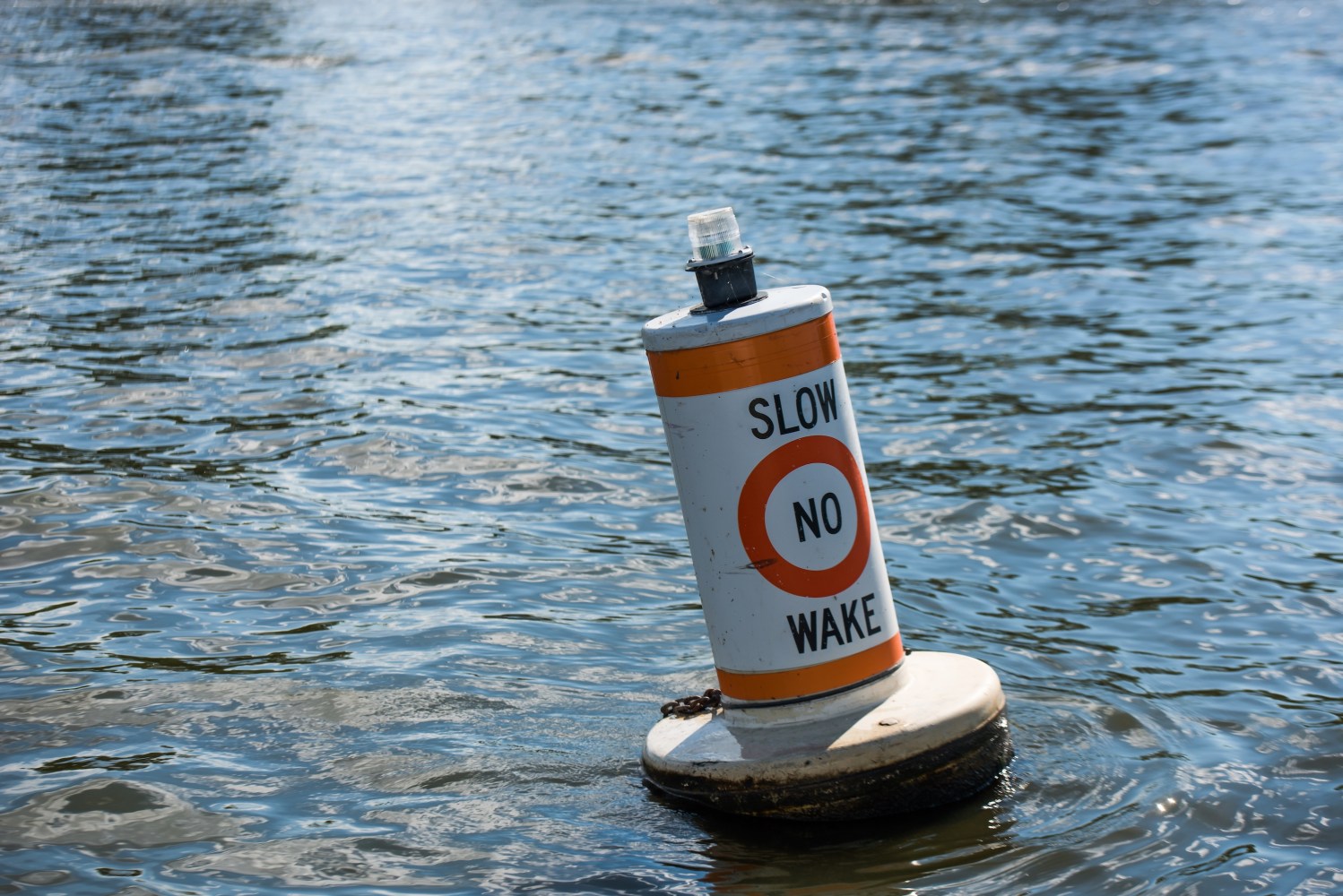 A buoy on water with text 'Slow No Wake' in orange and white.